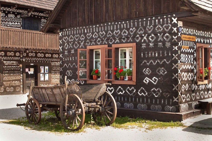 Puinen rakennus, jossa on koristeellisia kuvioita, ja sen edessä puinen kärry. 1