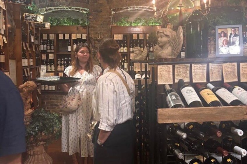 A wine cellar with shelves of bottles, a statue, and a sign. 3