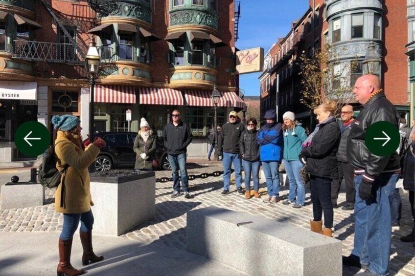 A group of people standing on a sidewalk in an urban area with buildings and a street sign. 5