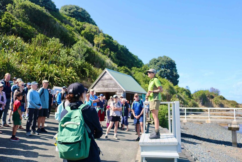 A group of people standing on a path near a wooden structure with a green roof, surrounded by lush green hills. 5