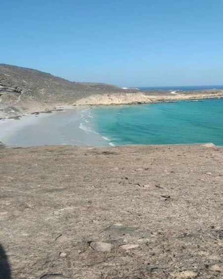 A coastal landscape with a beach, rocky terrain, and a clear sky. 4