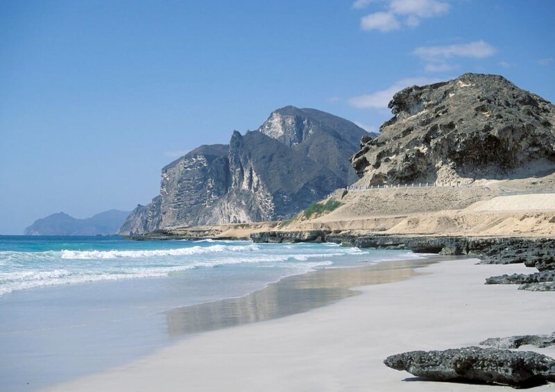 A beach with clear blue water, sandy shore, and rocky cliffs. 3