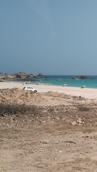 A white car parked on a rocky beach with a clear blue sky. 1