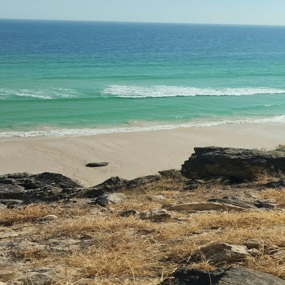A beach with clear turquoise water, sandy shore, and rocky outcrops. 3