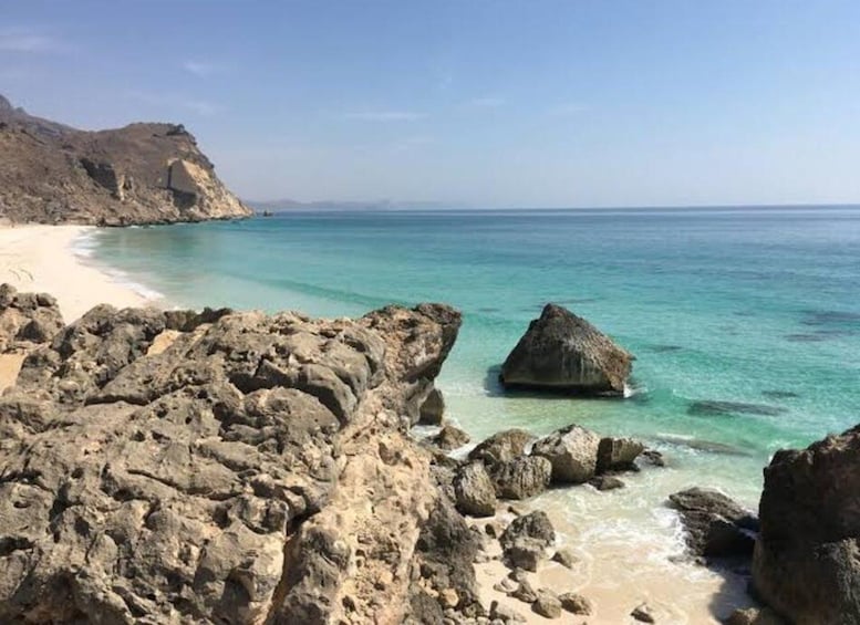A rocky shoreline with clear turquoise water and a sandy beach. 5