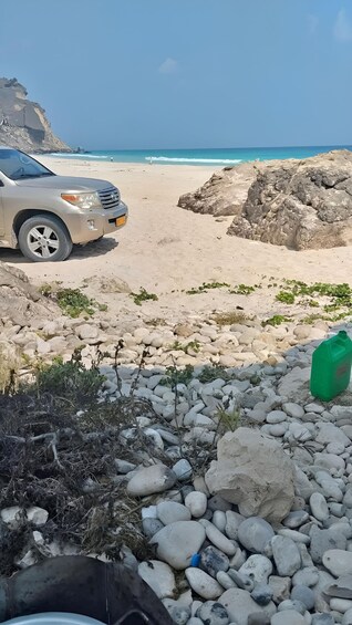 A beach with a car parked on the sand, rocks, and a green container. 2