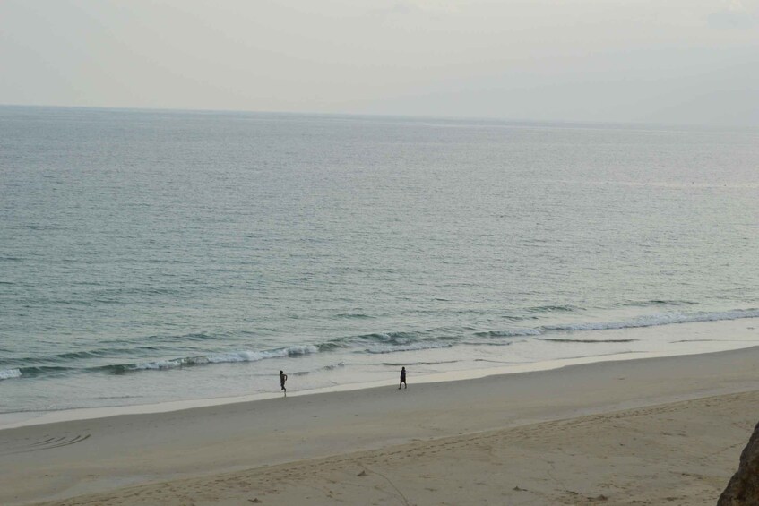 A beach with two people walking along the shore. 2