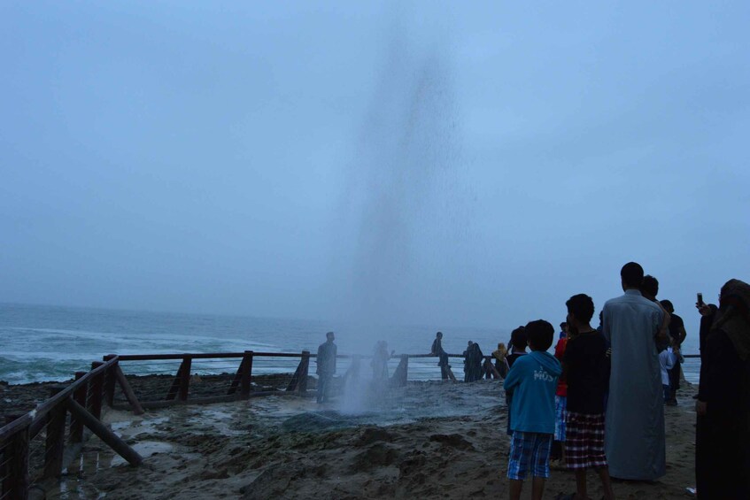 A group of people observing a geyser on a beach. 5