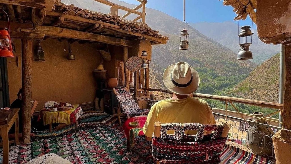 A traditional wooden hut with a thatched roof, a woven rug, and a person wearing a hat. 1