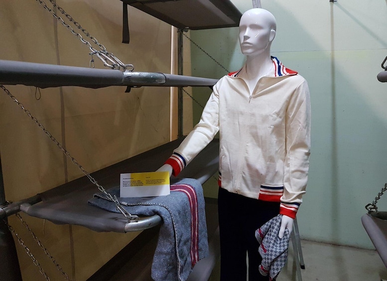 A mannequin dressed in a white jacket with red and blue stripes, holding a check and a checkered cloth. 1