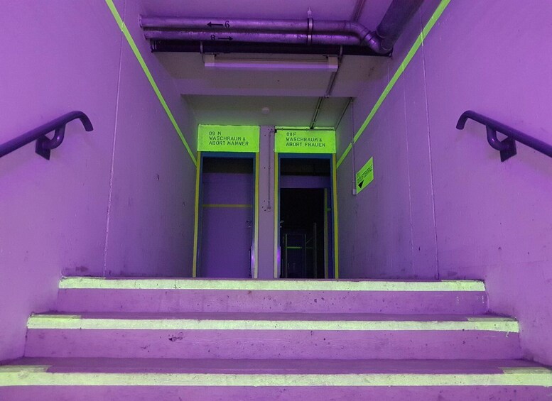 A set of purple stairs leading to a door with signs indicating '09 M WASHROOM & ABORT MANNER' and '09 F WASHROOM & ABORT FRAUEN'. 3