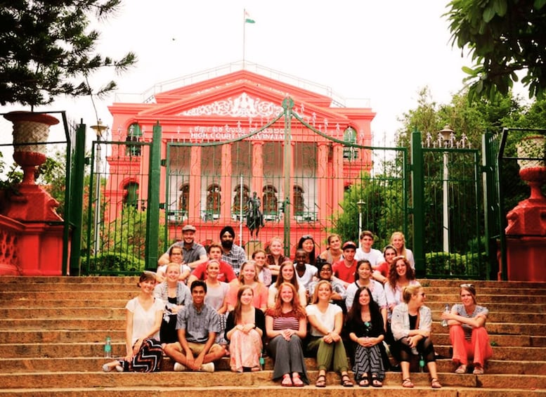 A group of people sitting on steps in front of a red building with ornate architecture and a flag. 3