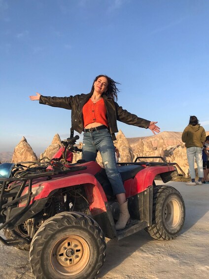 A person on a red ATV with a clear sky and rocky terrain in the background. 5