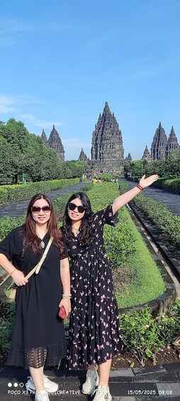 Two people standing in front of a temple with spires, surrounded by greenery. 2