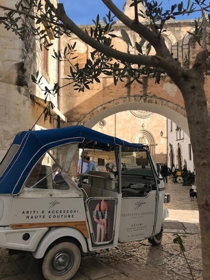 A vintage car parked under an archway with people in the background. 3