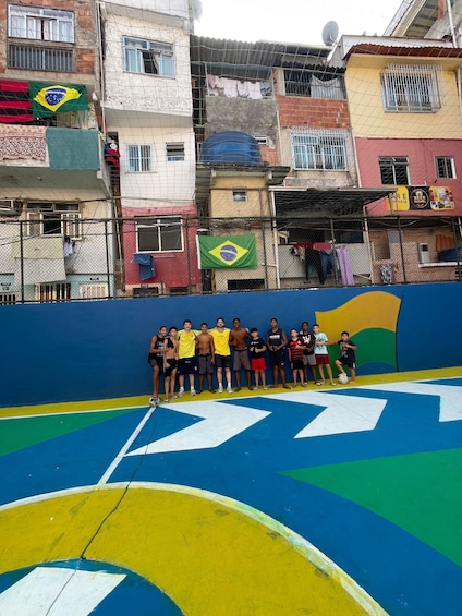 A group of people standing in front of a colorful wall with a Brazilian flag and a sports field with directional arrows. 2