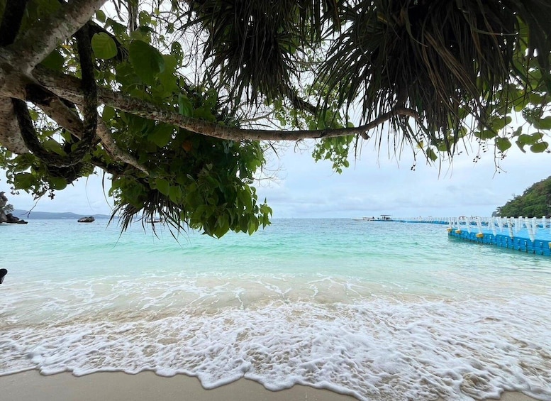 A beach with clear turquoise water, gentle waves, and a boat dock. 4