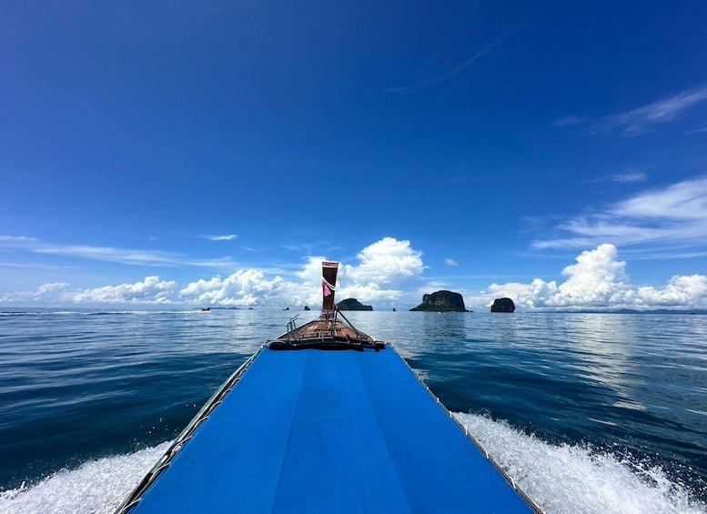 A boat with a blue hull and a wooden bow, sailing on calm blue waters with a clear sky and distant islands. 2