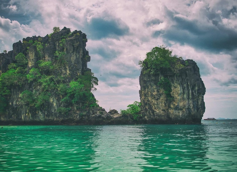 A coastal landscape with two prominent rock formations covered in greenery, surrounded by turquoise waters. 3