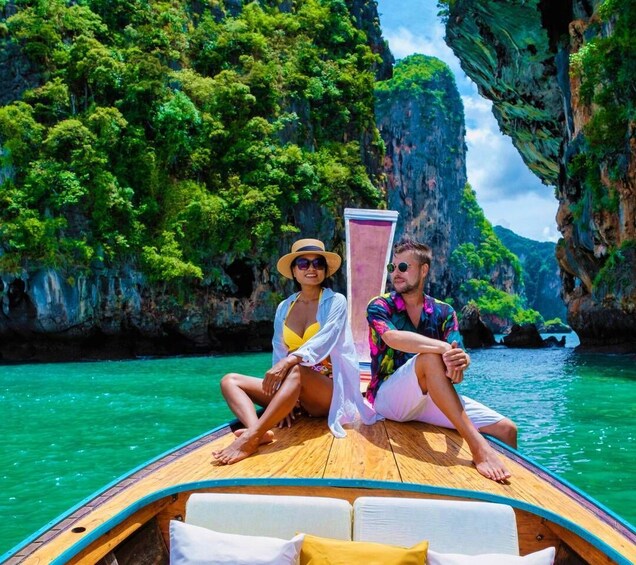 A couple on a boat in a clear turquoise sea with rocky cliffs and lush greenery in the background. 1