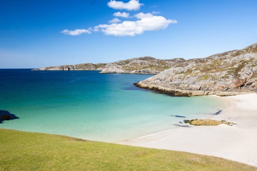 A coastal landscape with a clear blue sea, sandy beach, and rocky hills. 3