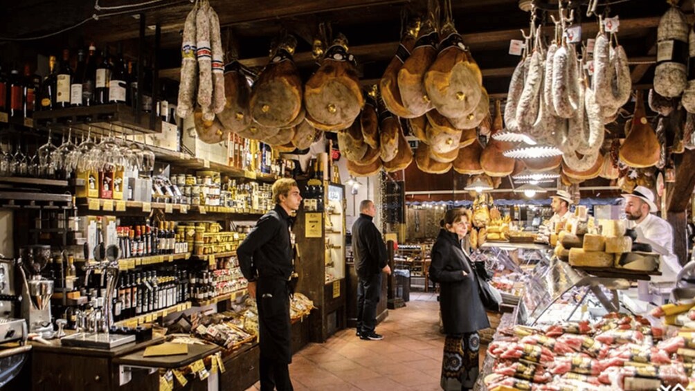 A market with hanging cured meats, shelves of bottled beverages, and a variety of packaged goods. 2