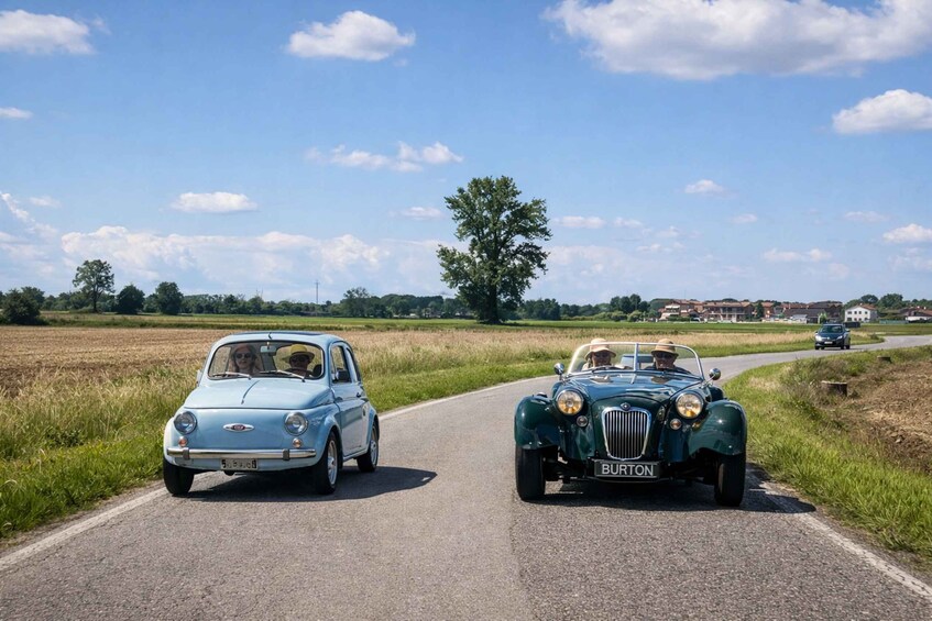 Two vintage cars driving on a rural road. 3