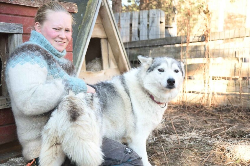 A person sitting next to a large dog in an outdoor setting with a wooden structure and a fence in the background. 2