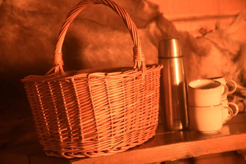 A wicker basket, a stainless steel thermos, and two white mugs on a wooden shelf. 5