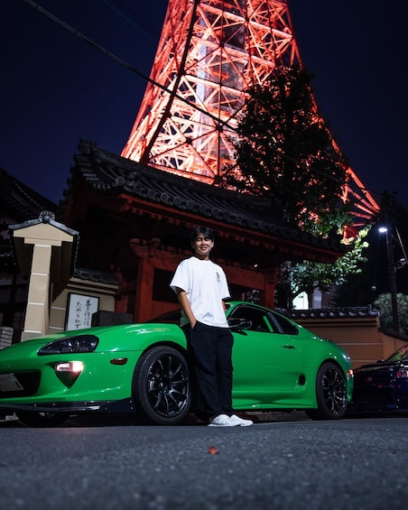 A person standing next to a green sports car with a Ferris wheel in the background. 5