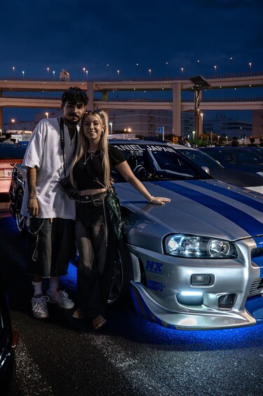 Two people standing next to a modified car with blue stripes and a spoiler. 1