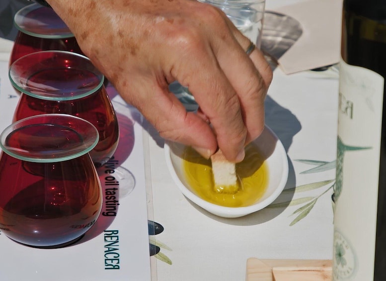A hand dipping a piece of bread into a bowl of oil. 5