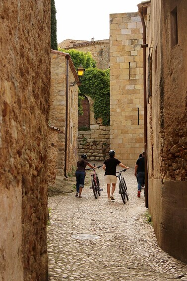 A narrow cobblestone street flanked by stone buildings, with cyclists and pedestrians. 1