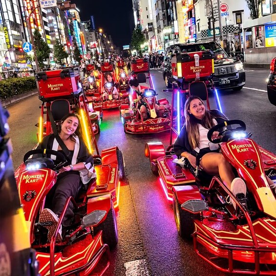 People driving Monster Kart go-karts on a city street at night. 1