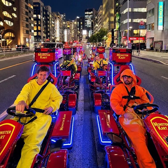 A group of people driving Monster Kart vehicles on a city street at night. 5