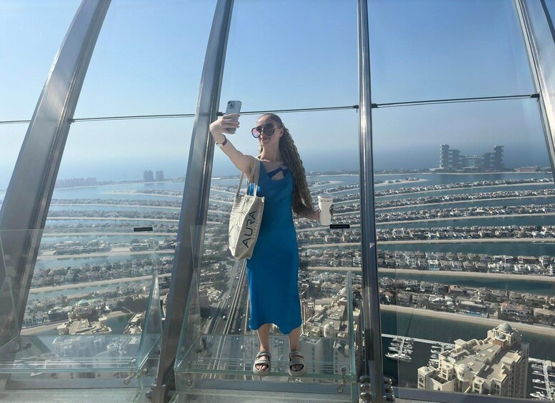 A person taking a selfie on a glass floor of a high-rise building with a cityscape view. 5