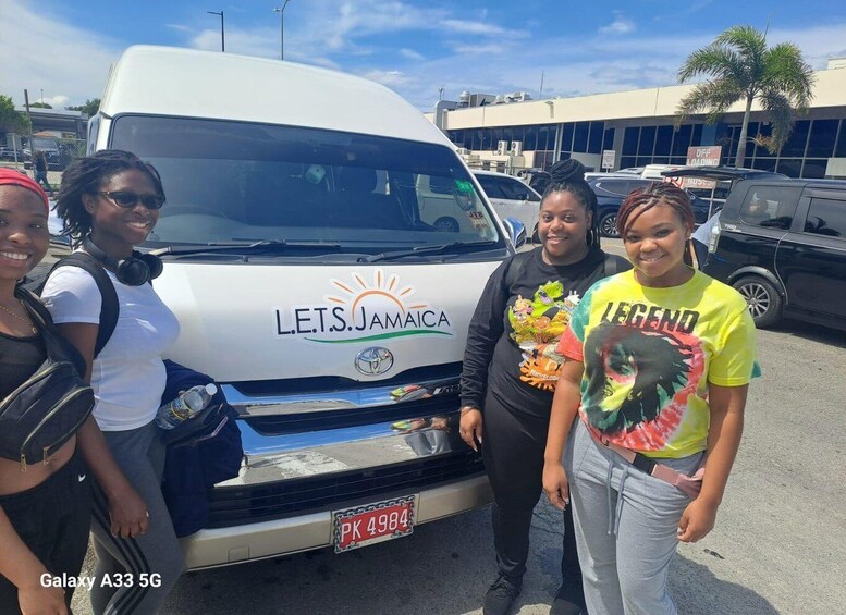 A white van with 'LET'S JAMAICA' and a sun logo, parked in a lot with other vehicles. 2