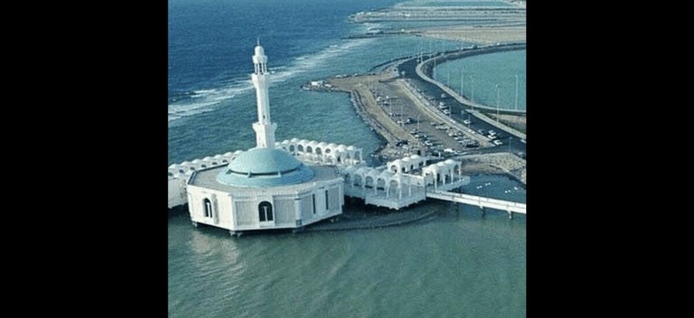 A mosque with a dome and minaret, surrounded by water and a coastal road. 2