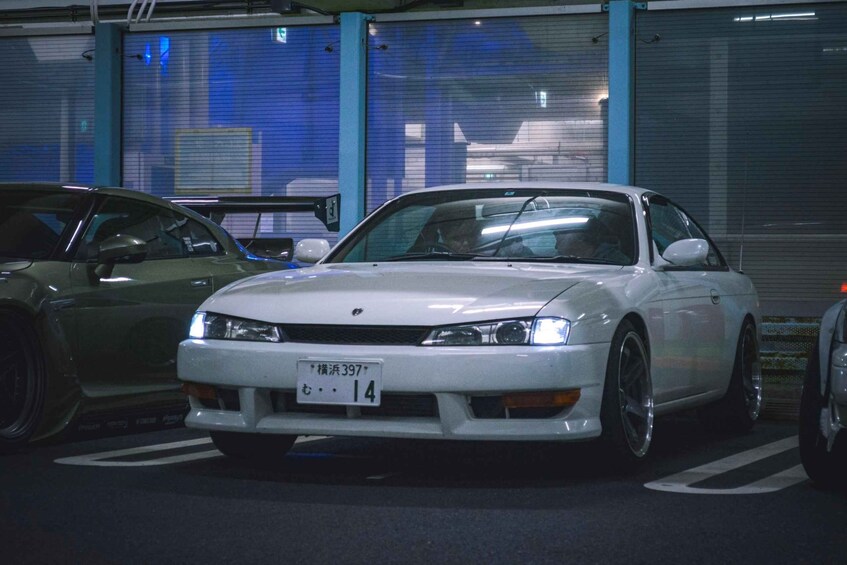 A white sports car parked in a garage with blue walls and a closed garage door in the background. 2