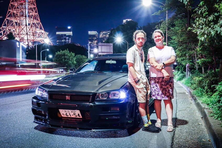 A black sports car parked on a city street at night with illuminated buildings in the background. 2