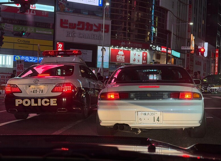 Two police cars with visible license plates and a city street at night with illuminated signs. 5