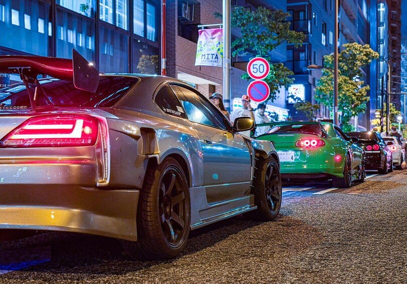 A street at night with a sports car parked on the side, a speed limit sign, and other vehicles. 4