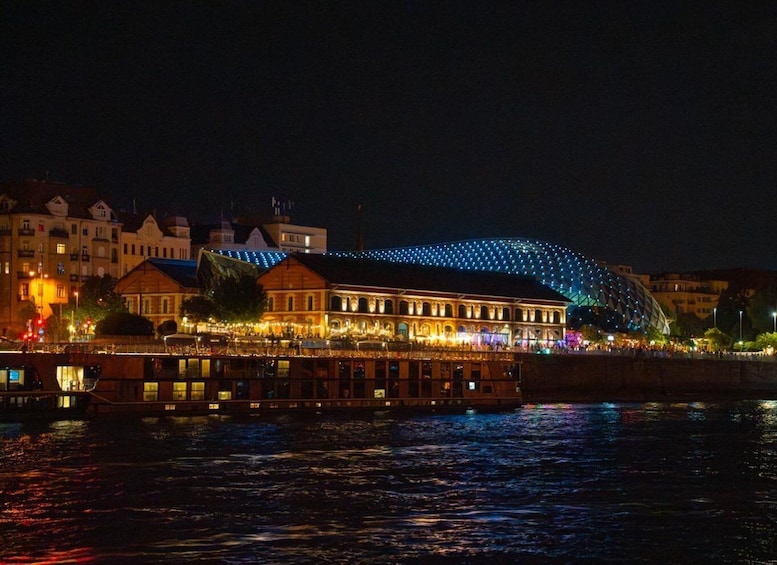 A waterfront with illuminated buildings and a boat docked in the foreground. 5