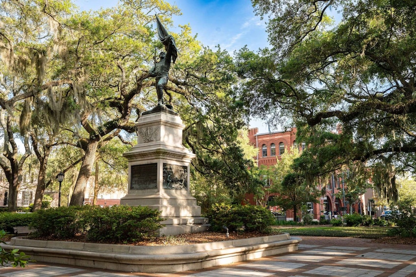 A statue in a park with trees and a brick building in the background. 5