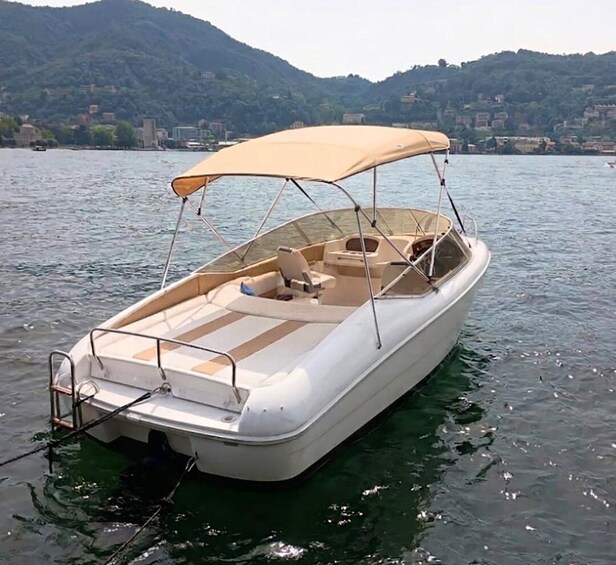 A small motorboat with a canopy, docked on calm water with hills in the background. 1