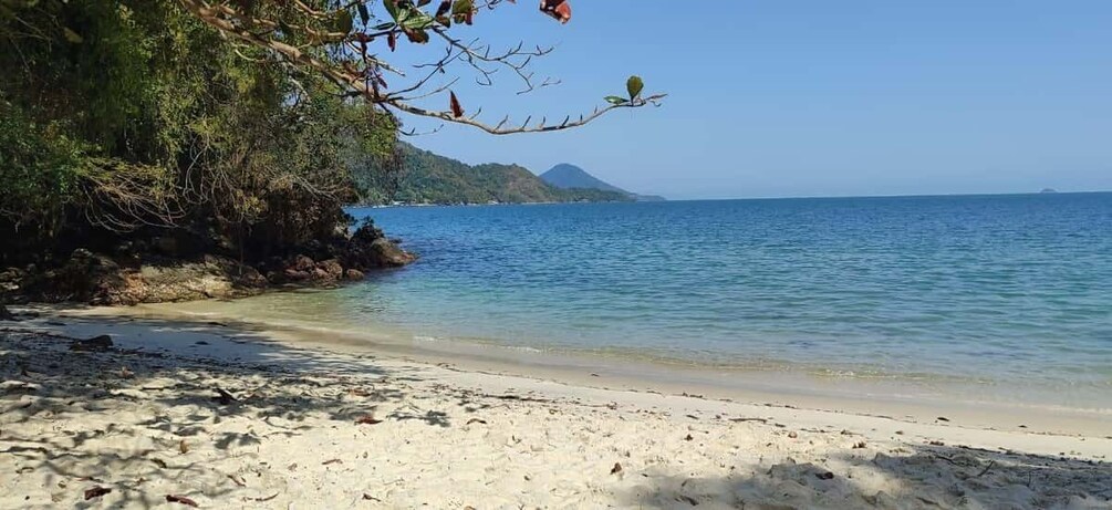 A beach with clear water, sandy shore, and a mountain in the background. 1