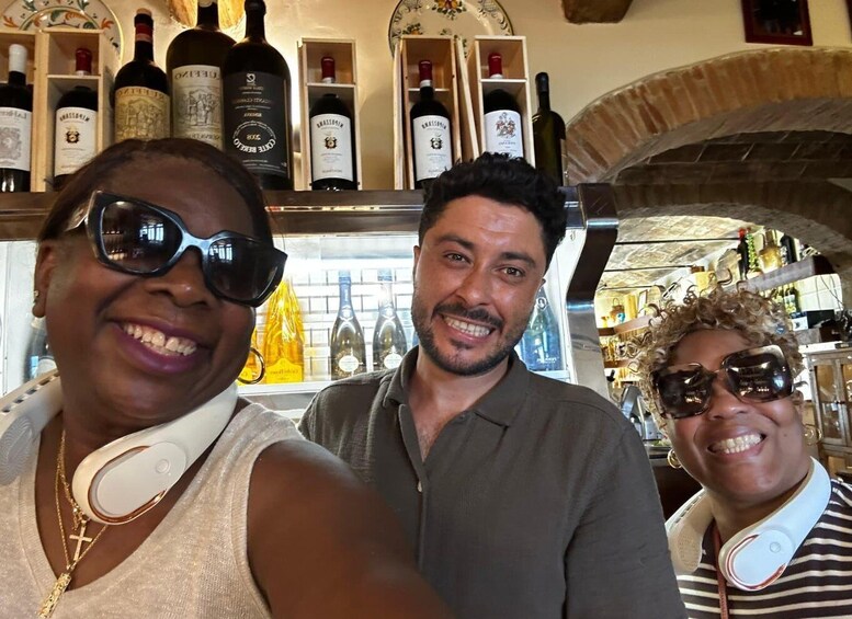 Three people in a bar with shelves of wine bottles. 5