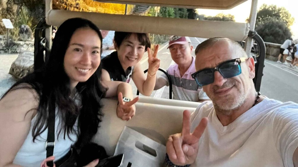 A group of people in a vehicle, possibly a golf cart, with a natural landscape in the background. 2