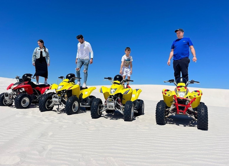 A group of people standing on a sandy dune with quad bikes. 5