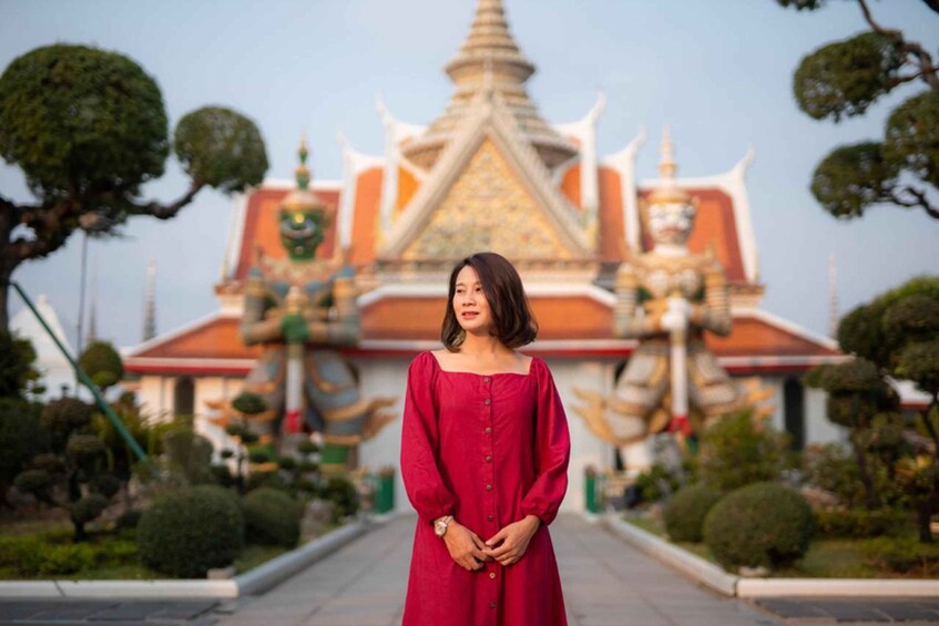 A woman in a red dress standing in front of a temple with a golden spire and intricate architecture. 1